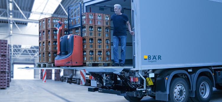 Un autista di camion scarica un pallet di bevande e un carrello elevatore elettrico con una sponda montacarichi BAR in un capannone