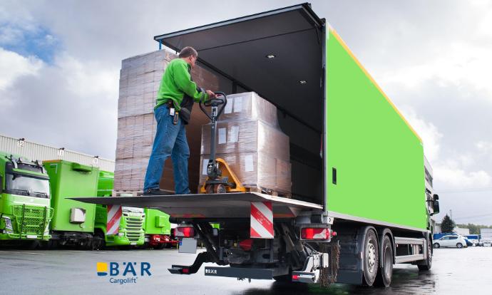 Un autista di camion spinge i pallet con un transpallet dalla piattaforma BAR Lift nel camion